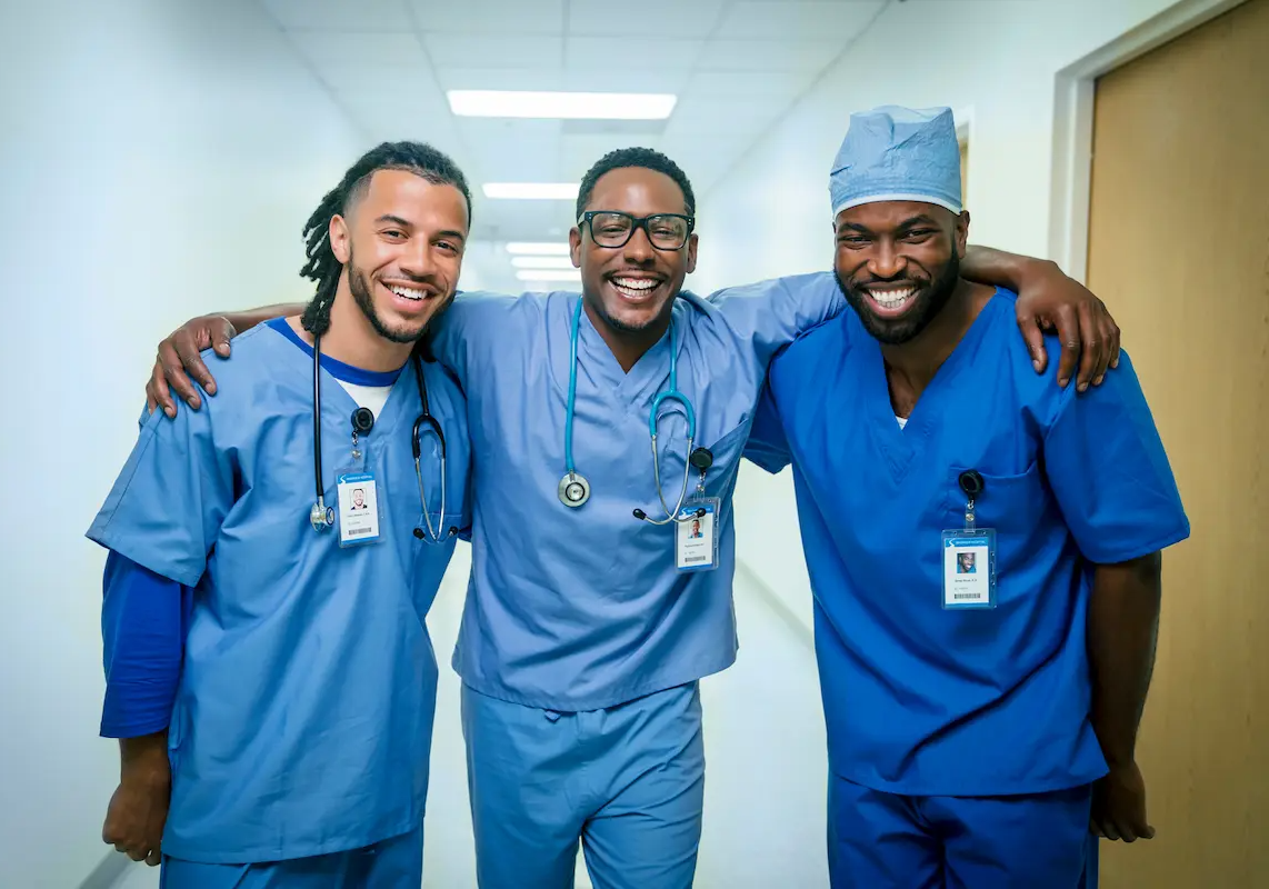Three healthcare workers smiling and standing together in a hospital hallway