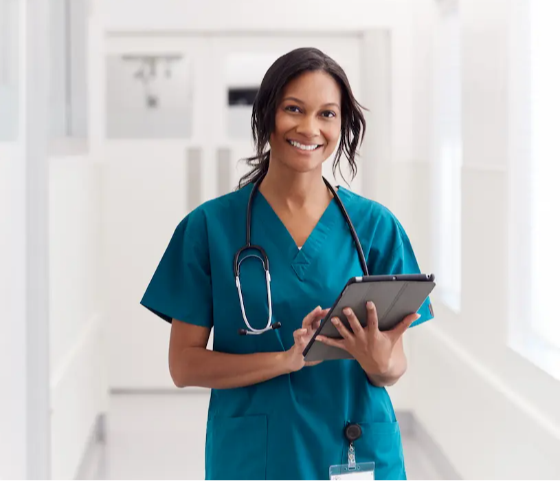 A RN smiling and holding a tablet while in a hospital hallway