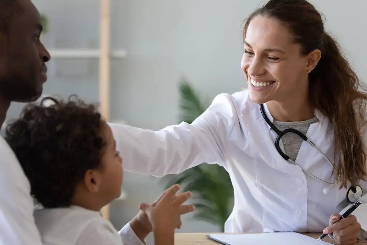 NP smiling with a child and parent patient NP smiling with a child and parent patient
