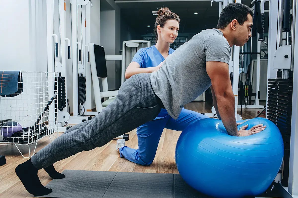 Physical therapy assistant helps a patient stretch with an exercise ball