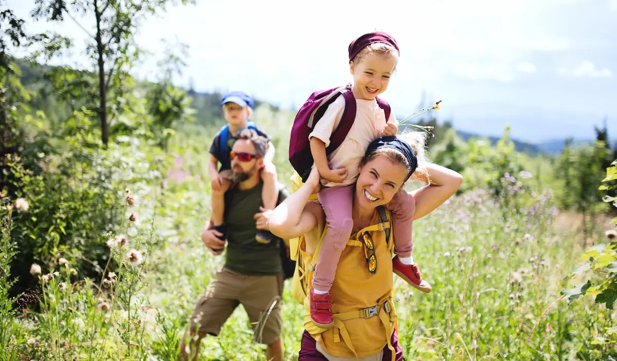 Two parents on PTO hiking in a field with their toddlers on their shoulders