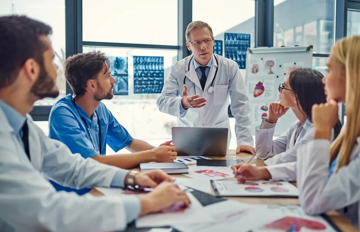 A group of physicians and allied health workers talking and sitting at a table in a conference room