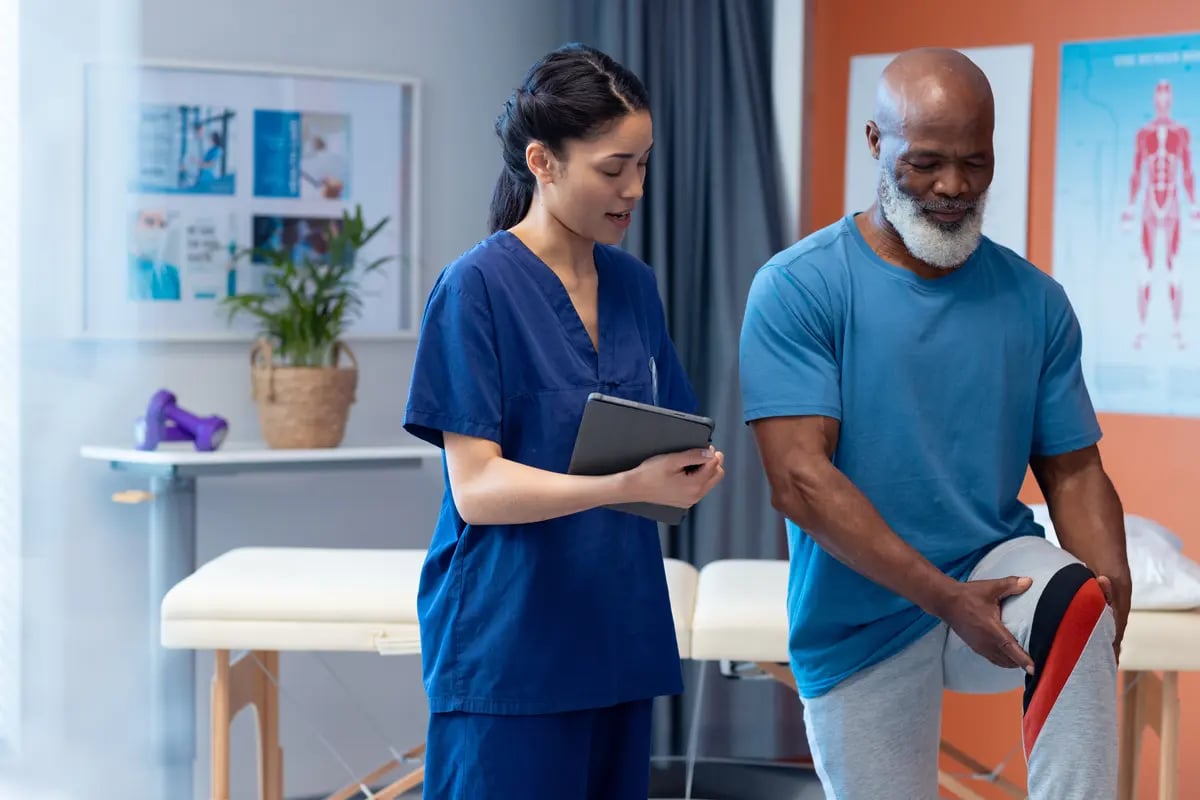 Direct hire physical therapist holding a tablet treating a patient at a rehab center