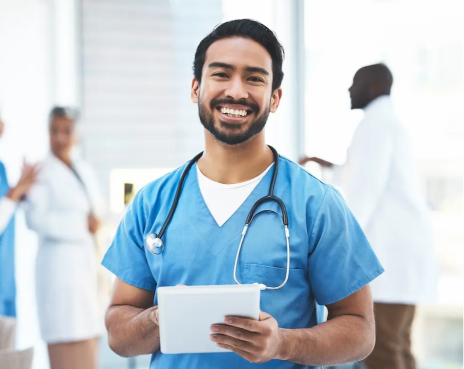 Male nurse with a full-time job smiling and holding a tablet with physicians in the background