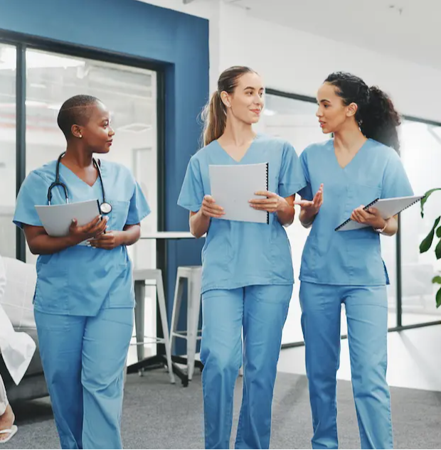 Three female RNs walking and chatting in a hospital lobby holding documents