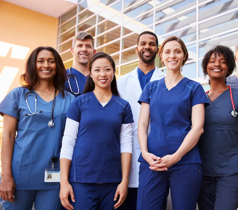 Group of physicians, nurses, and allied health professionals smiling for a group photo in a hospital lobby