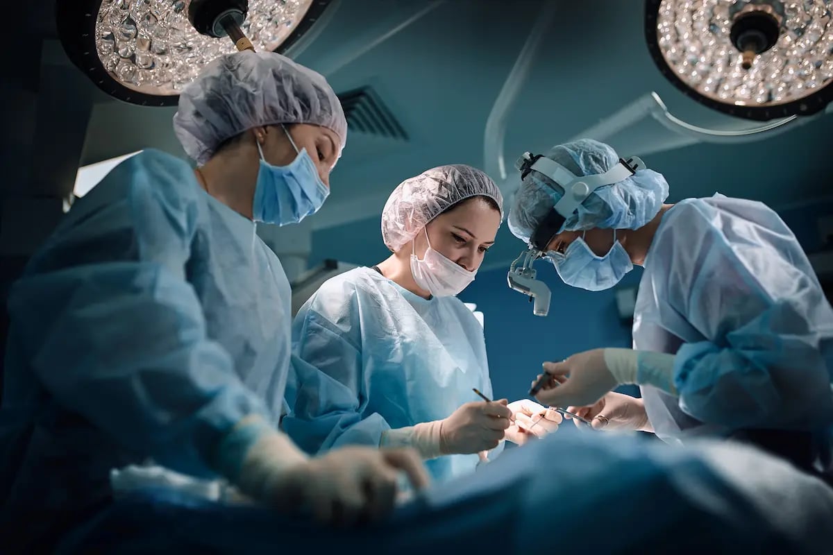 Three surgical techs prepping tools in a hospital operating room