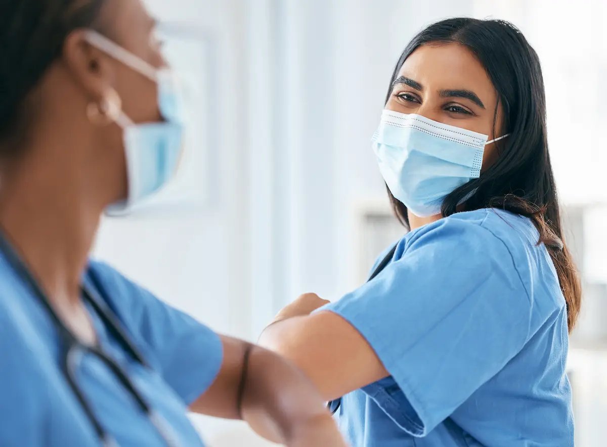 Two LPNs bumping elbows and wearing face masks in a long-term care facility