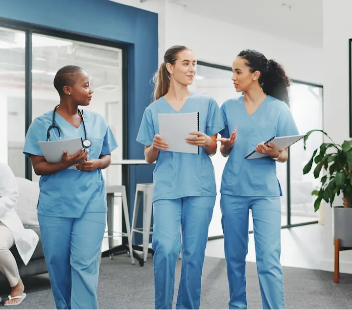 Three female RNs walking and chatting in a surgery center lobby holding documents