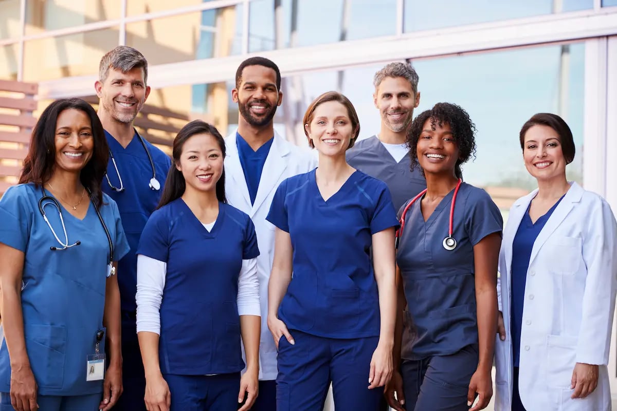 Group of physicians, advanced practice nurses, and RNs standing in front of a healthcare facility