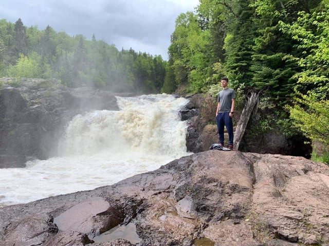 Travel RN stands on rocks near river's edge at Minnehaha Falls near Minneapolis, Minnesota