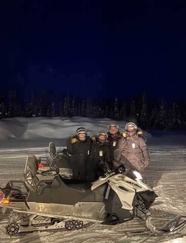 Travel nurses standing behind a snowmobile on a snowy road in Fairbanks, Alaska