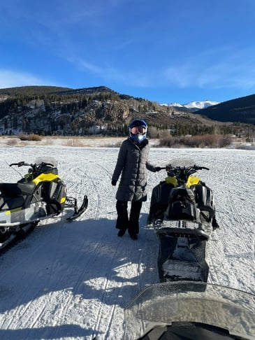 Travel RN stands next to a snowmobile in the mountains of Boulder, Colorado