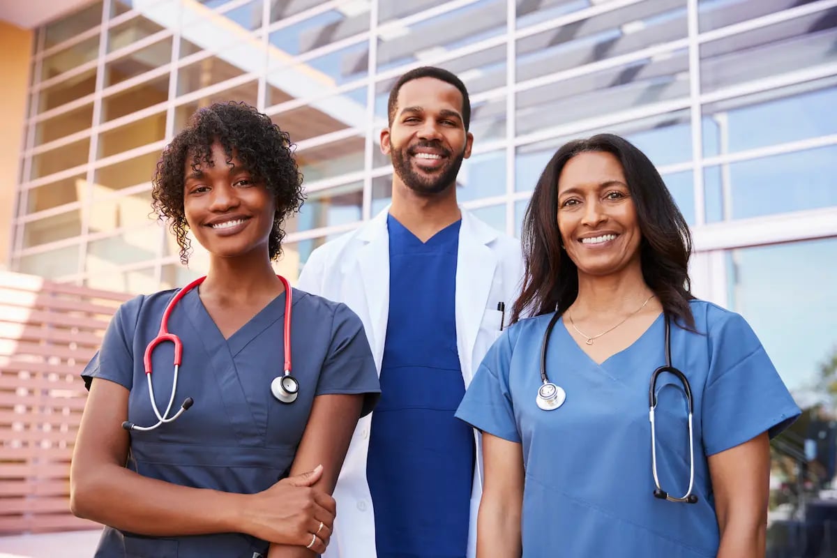 A physician and two nurses standing in front of a doctor's office