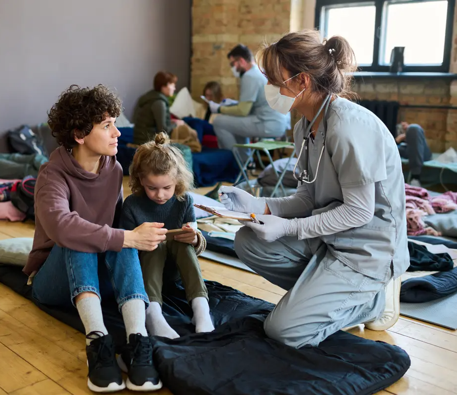 Emergency RN kneeling down talking to small children at a emergency shelter