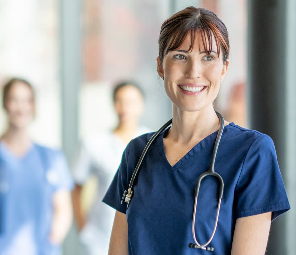 RN standing by a window in a hospital smiling with two other nurses in the background