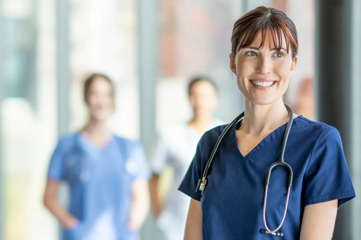 RN standing by a window in a hospital smiling with two other RNs in the background