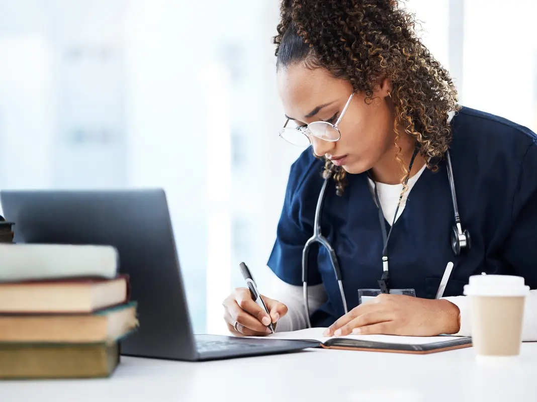 Healthcare student taking notes while continuing her nursing education sitting at a desk