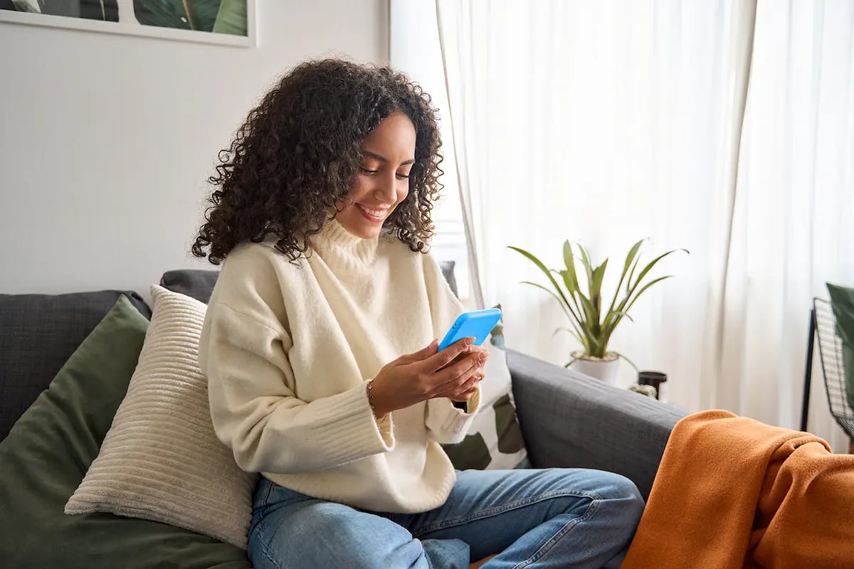 Per diem nurse sitting on a couch at home picking up shifts on her phone using Mobilize, powered by Favorite Healthcare Staffing