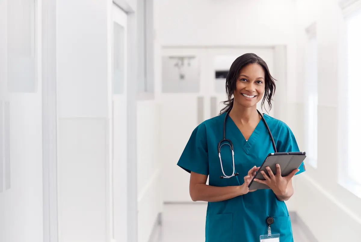 A registered nurse standing in a healthcare facility smiling and holding a tablet