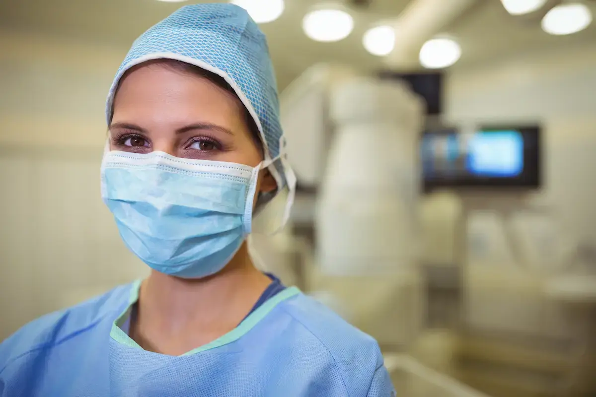 Interventional radiology tech standing in front of a CT machine wearing a mask