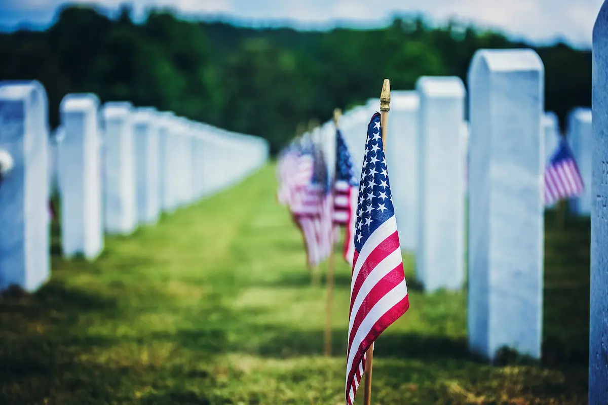 Several rows of tombstones with American flags in front of them honoring veterans 