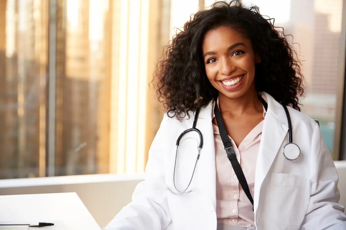 A nurse practitioner smiling and sitting at a desk with a stethoscope around her neck