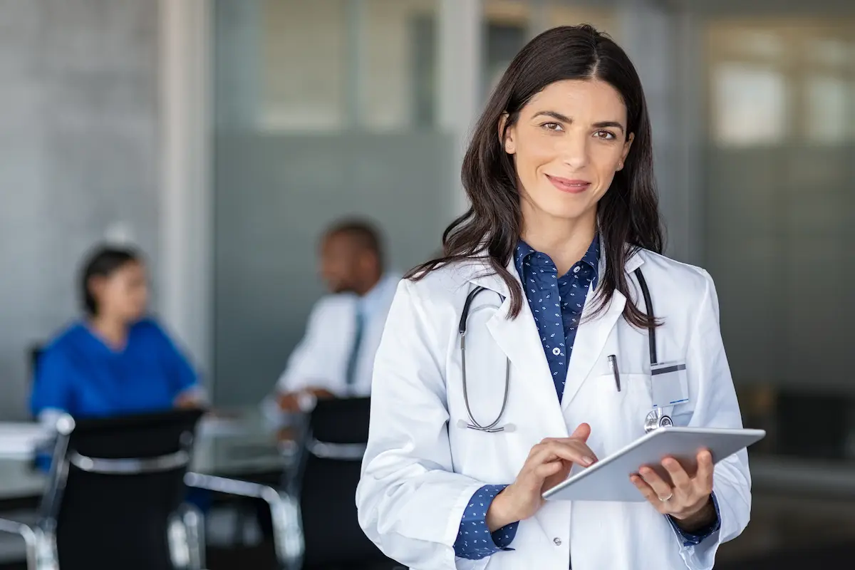 A per diem nurse practitioner standing in a healthcare facility holding a tablet