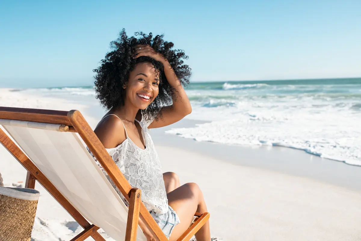 A travel nurse lounging and smiling in a beach chair by the ocean 