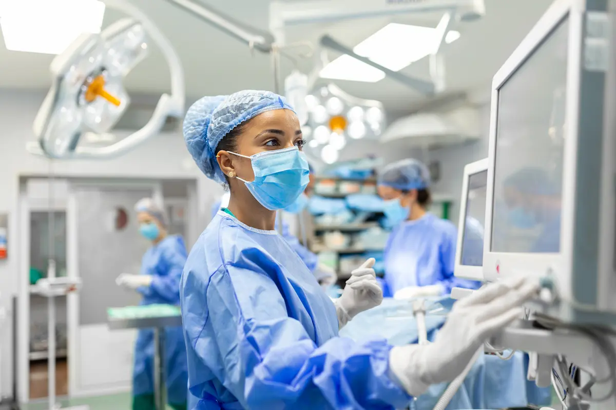 An allied health professional touching a monitor in an operating room