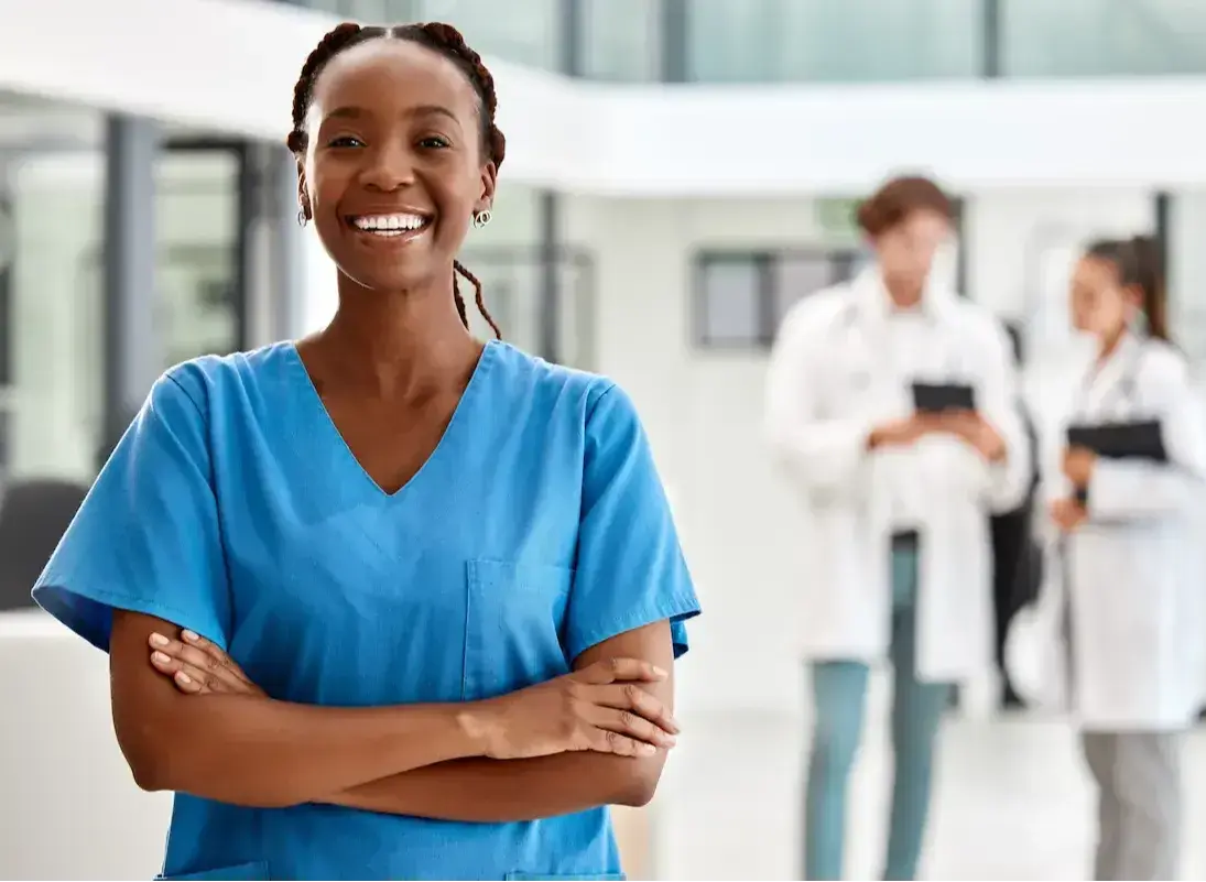 Travel nurse smiling and crossing her arms while standing in a hospital lobby