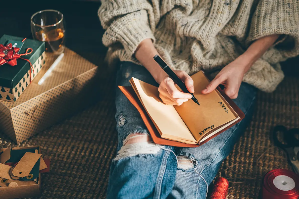 A woman sitting on the floor writing down her goals for the new year