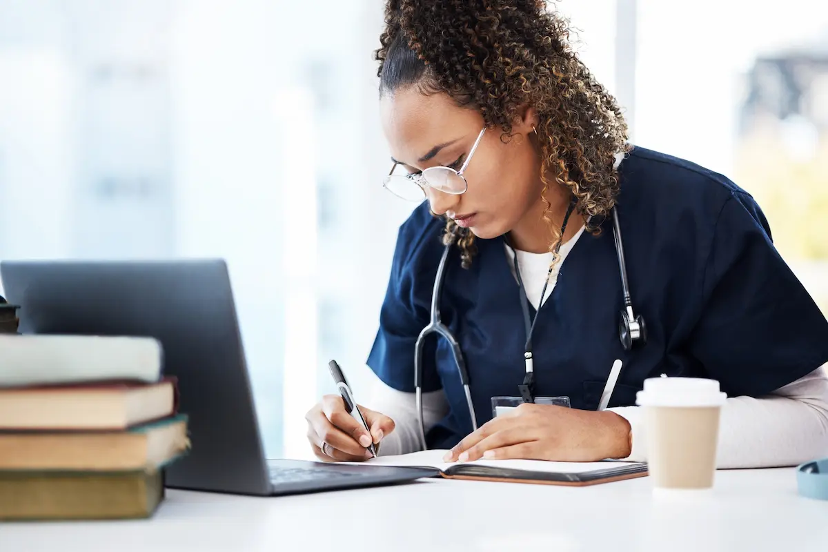 Student studying to become a nurse by writing notes off of a laptop