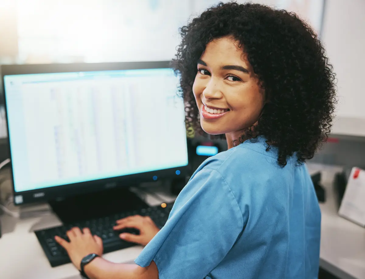 Non-clinical hospital receptionist smiling while typing on her computer at her desk