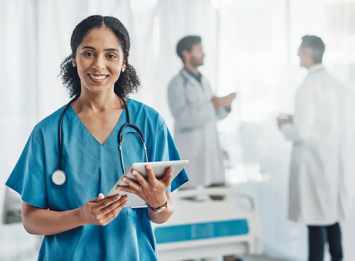 Nurse smiling and holding a tablet while in a hospital room