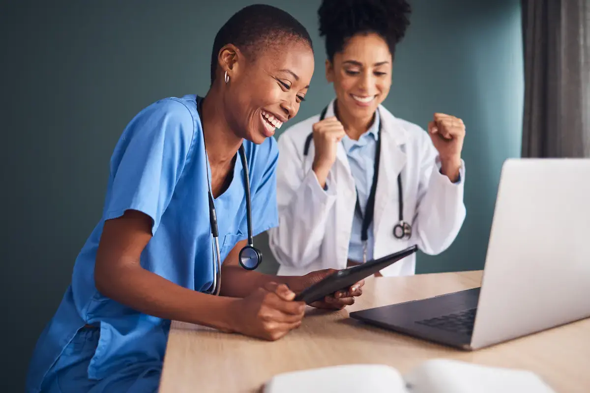 A physician and a per diem CNA smiling and working at a tablet and laptop