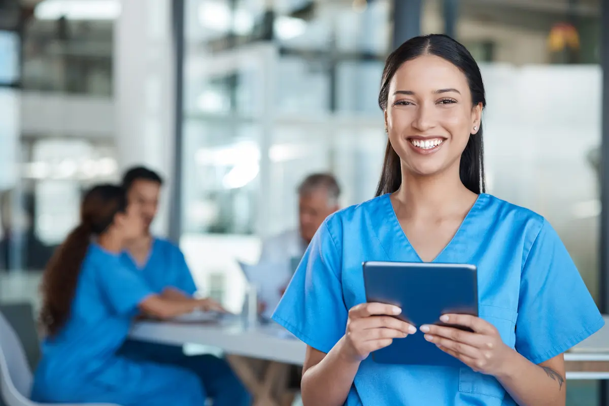 Registered Nurse Smiling and Holding a Tablet Standing in a Hospital Meeting Room