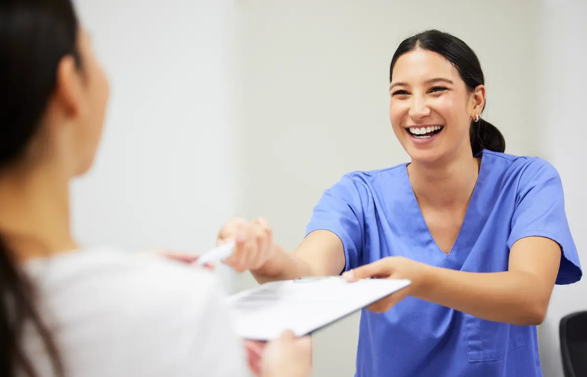 A medical assistant handing a patient paperwork and a pen