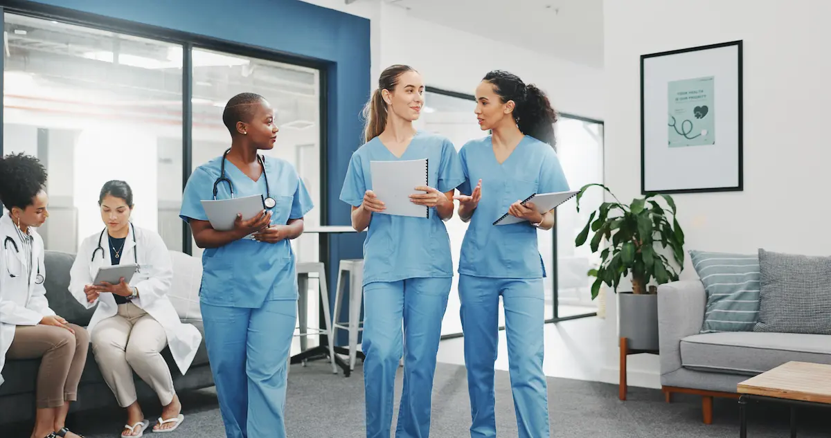 Three nurses walking through a hospital together while talking