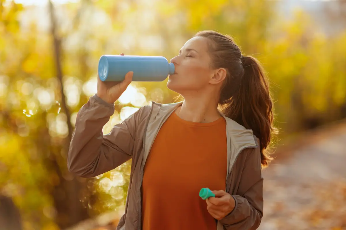 An off duty registered nurse drinking out of her water bottle while walking on a trail