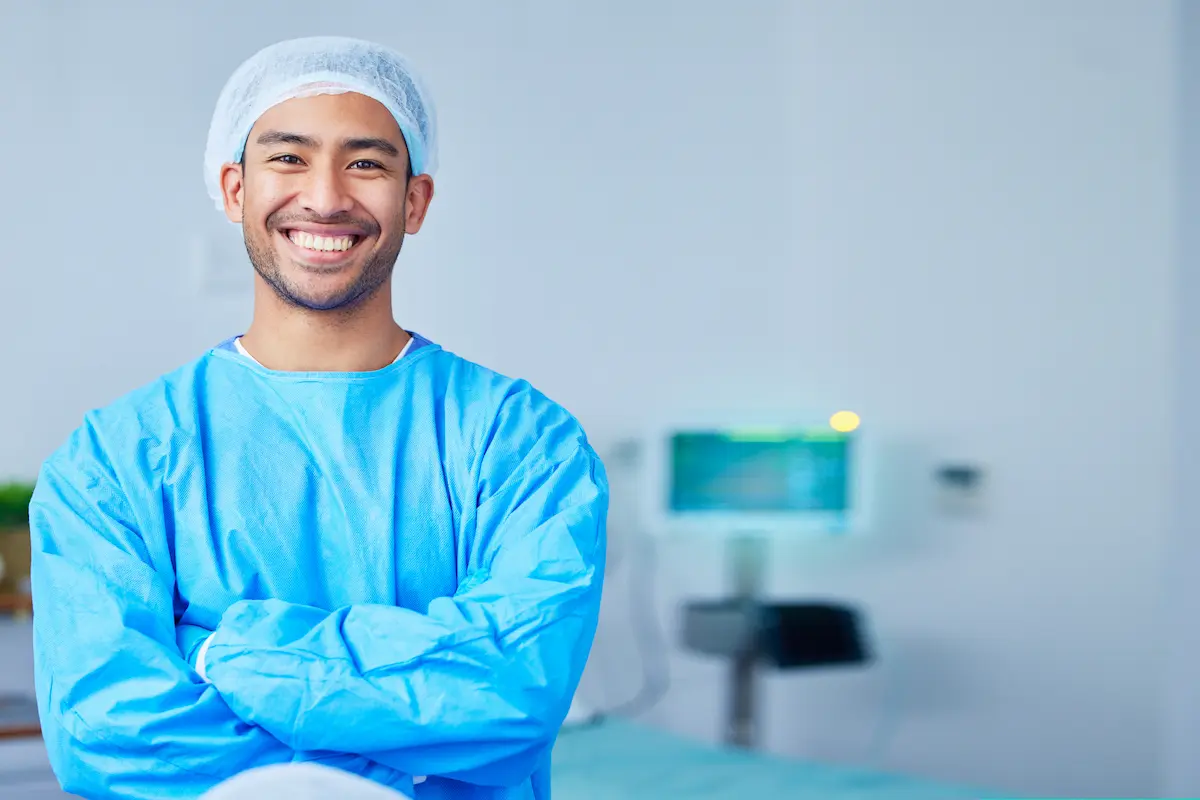 An allied health professional smiling with his arms crossed wearing surgical protective gear