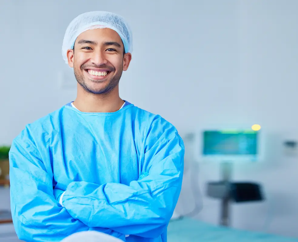 Allied health professional wearing medical protective equipment smiling with his arms crossed at the hospital