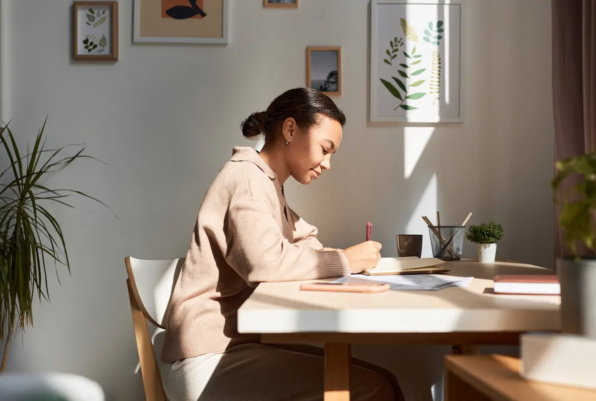 A female healthcare professional sitting at her desk at home writing in her journal