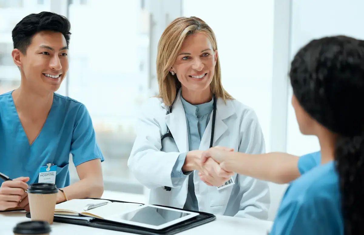 A IR tech and physician sit at a table and shake hands with another healthcare professional