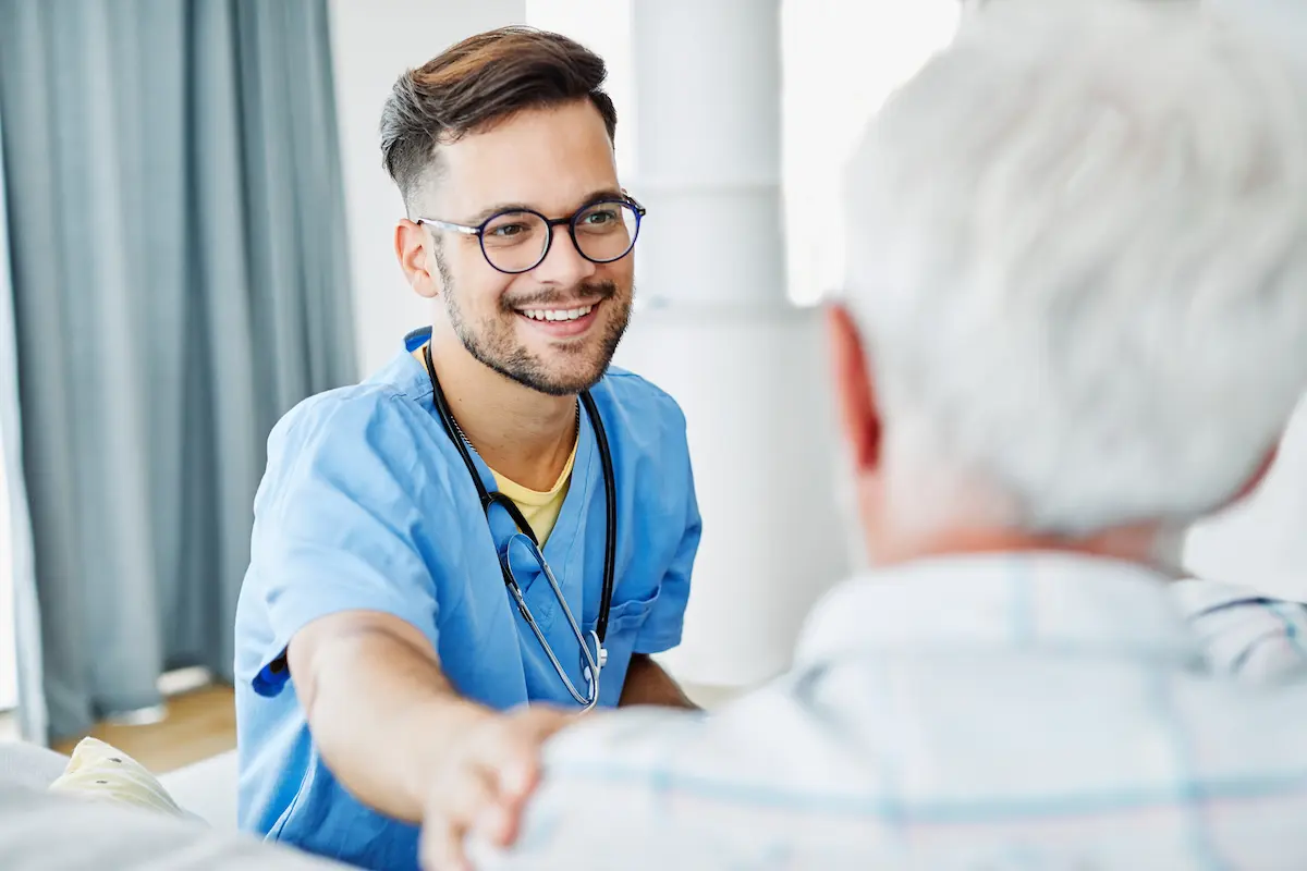 A male nurse smiling with his hand on an older male patients shoulder 