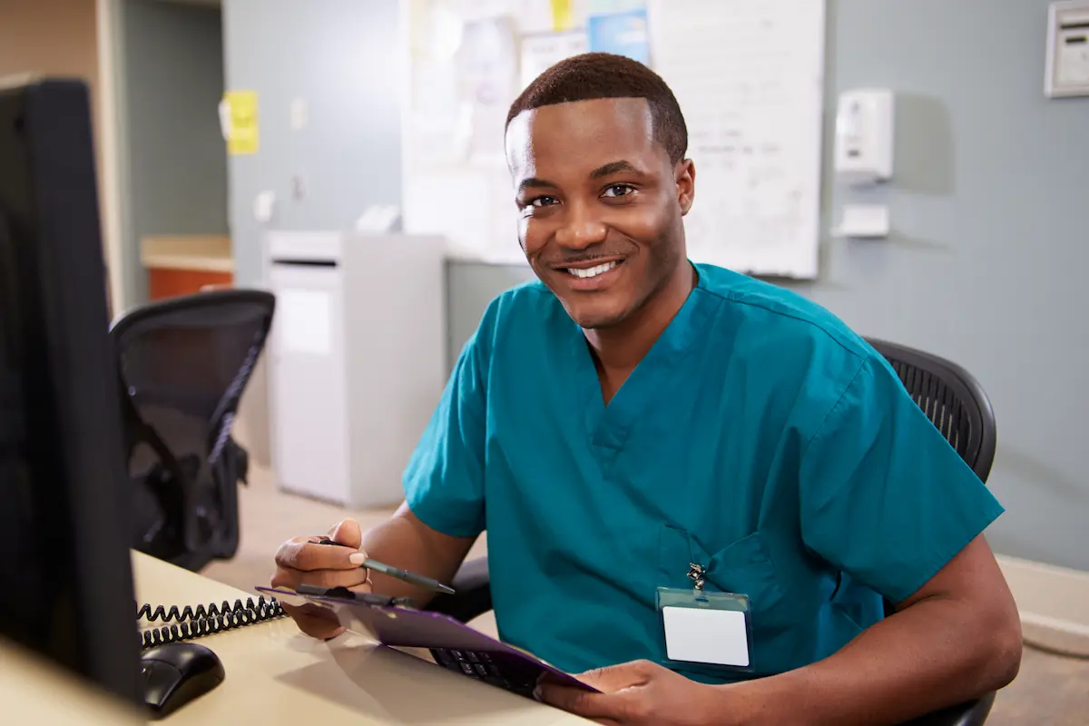 Full-time medical assistant sitting at a desk holding a clipboard in a physician's office