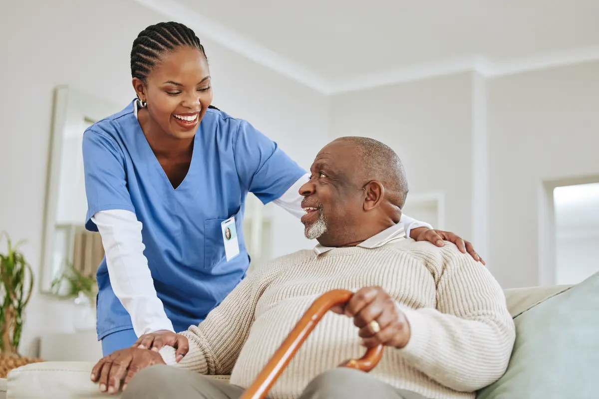 A per diem nurse smiling and helping an elderly patient in his home