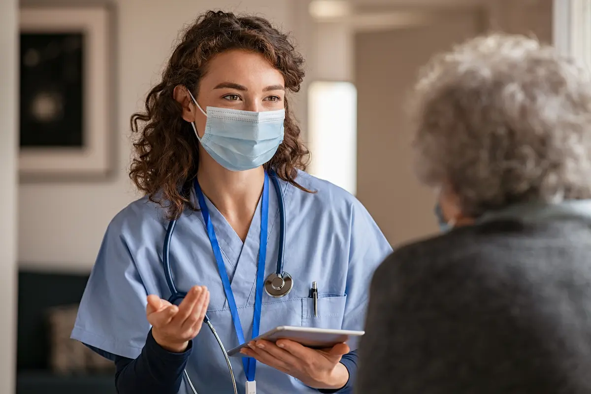 Per diem nurse wearing a mask working in a nursing home talking to an older patient
